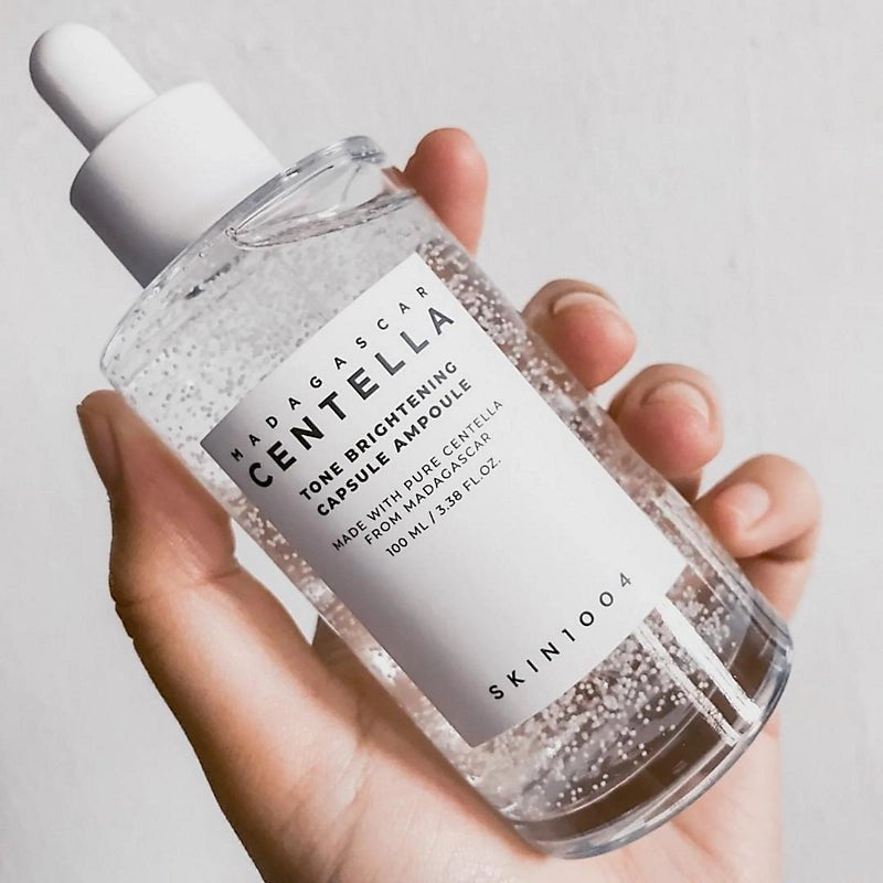 Hand holding a skincare bottle labeled 'Madagascar Centella' with a plain background
